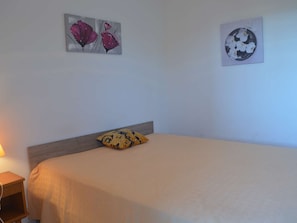 Quarto com cama, mesa de cabeceira e duas pinturas de flores na parede.
