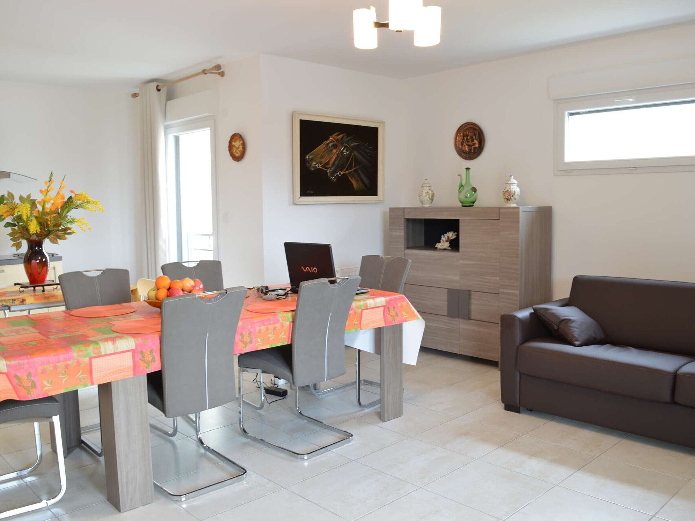 A modern dining area with a table set for four, a laptop on the table, and a sofa in the living area.