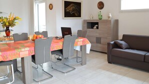 A modern dining area with a table set for four, a laptop on the table, and a sofa in the living area.