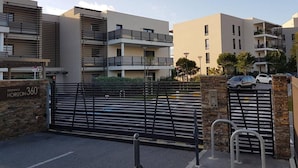 A gated residential complex with modern architecture, multiple balconies, and a parking area.