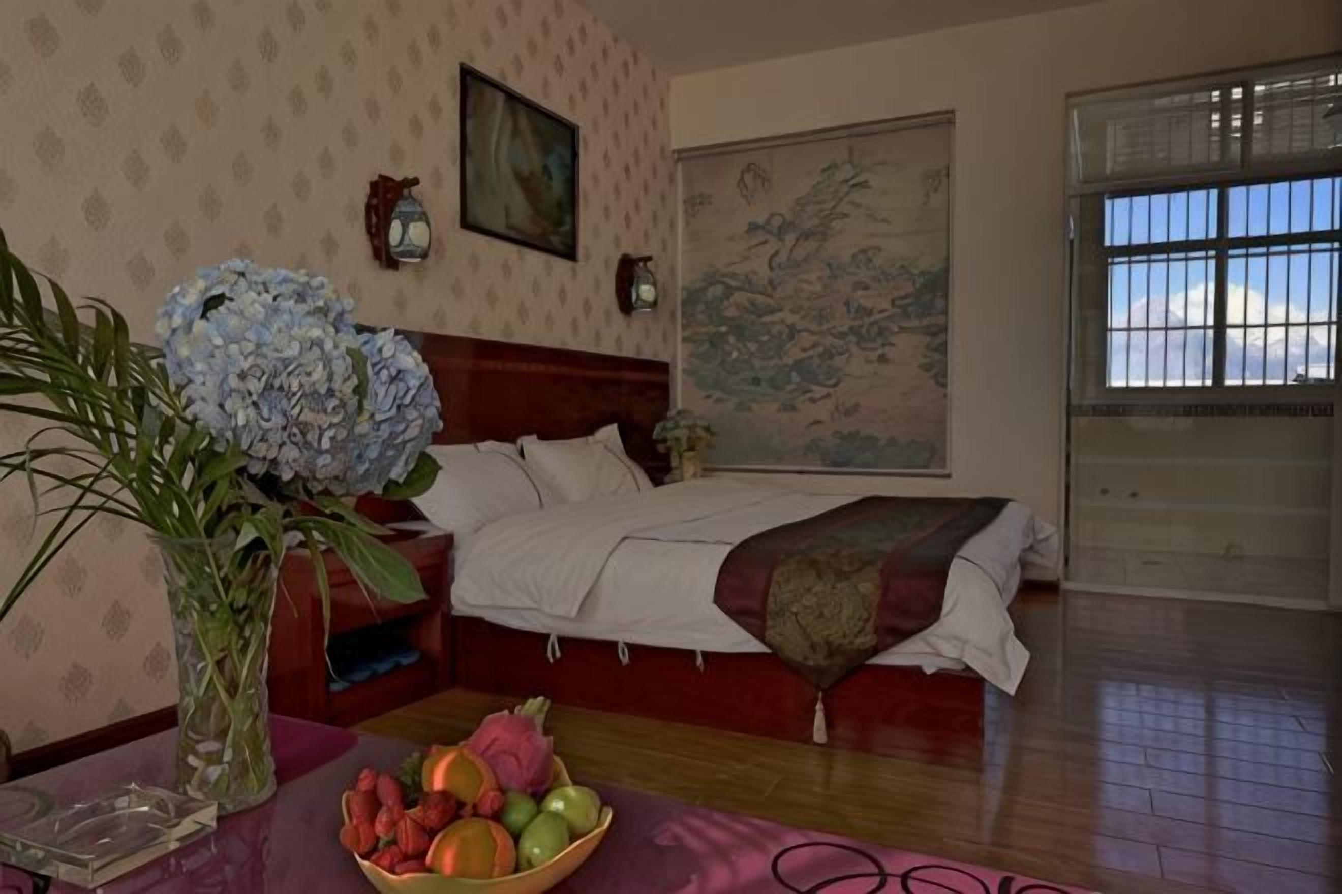 Un dormitorio con cama, mesita de noche, un jarrón con flores y frutero.