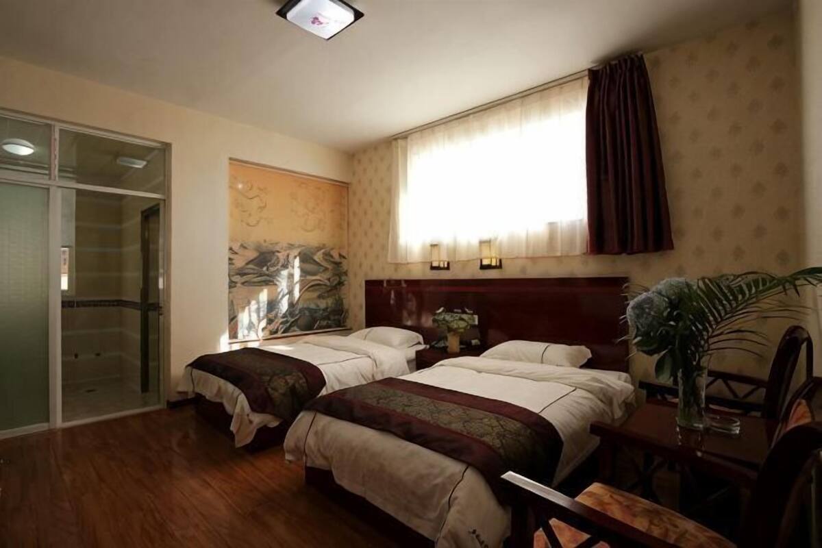 Habitació d'hotel amb dos llits, un sòl de fusta, una porta corredissa de vidre, un finestral gran amb cortines i una làmpada penjada a la paret.