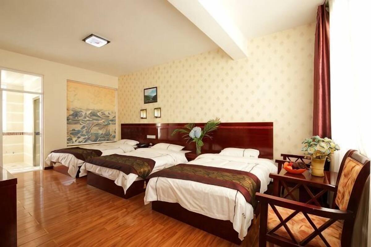 Habitació d'hotel amb tres llits, un sòl de fusta, una taula de treball amb cadira i una finestra gran.