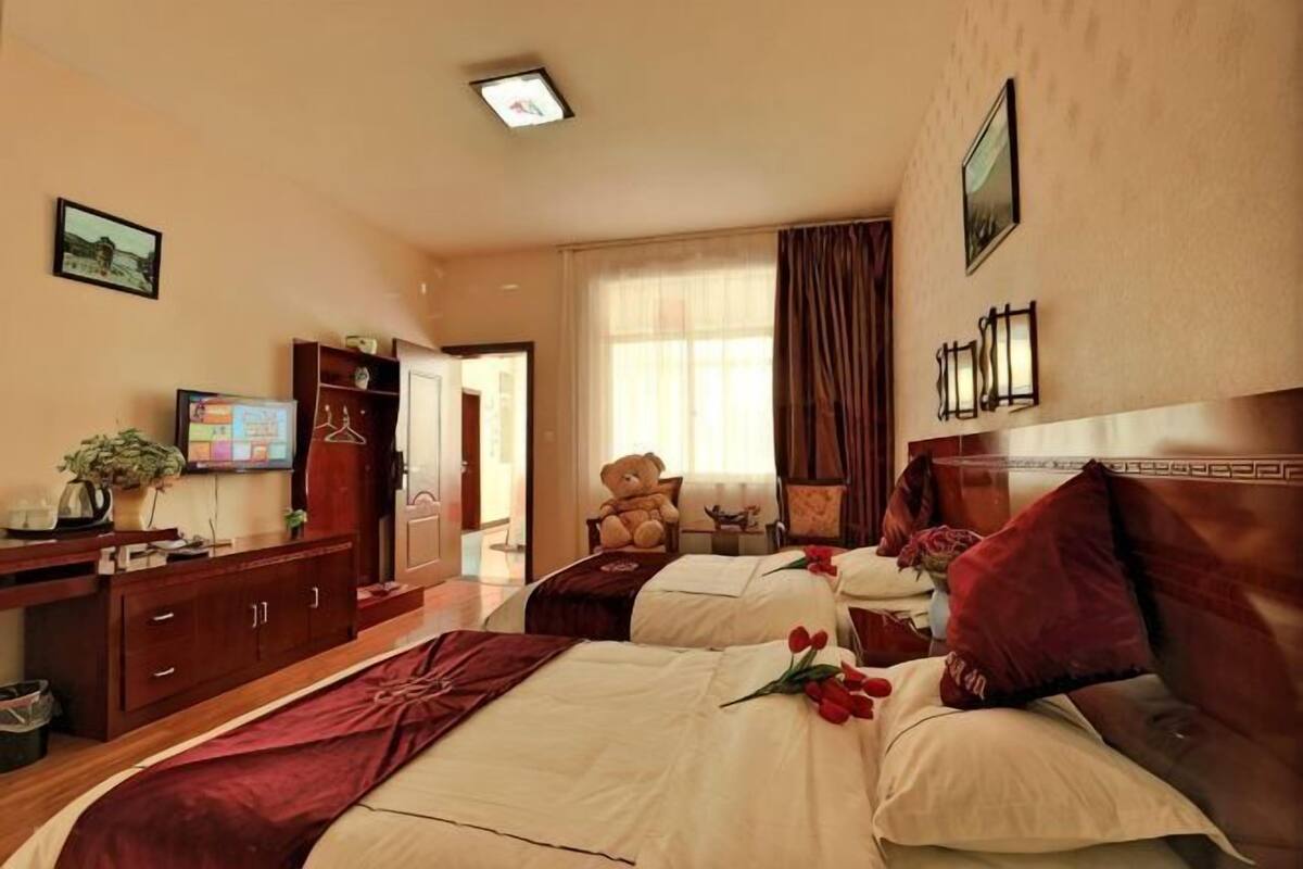 Una habitació d'hotel amb dos llits, un escriptori amb un ordinador, una televisió i un os de peluix.