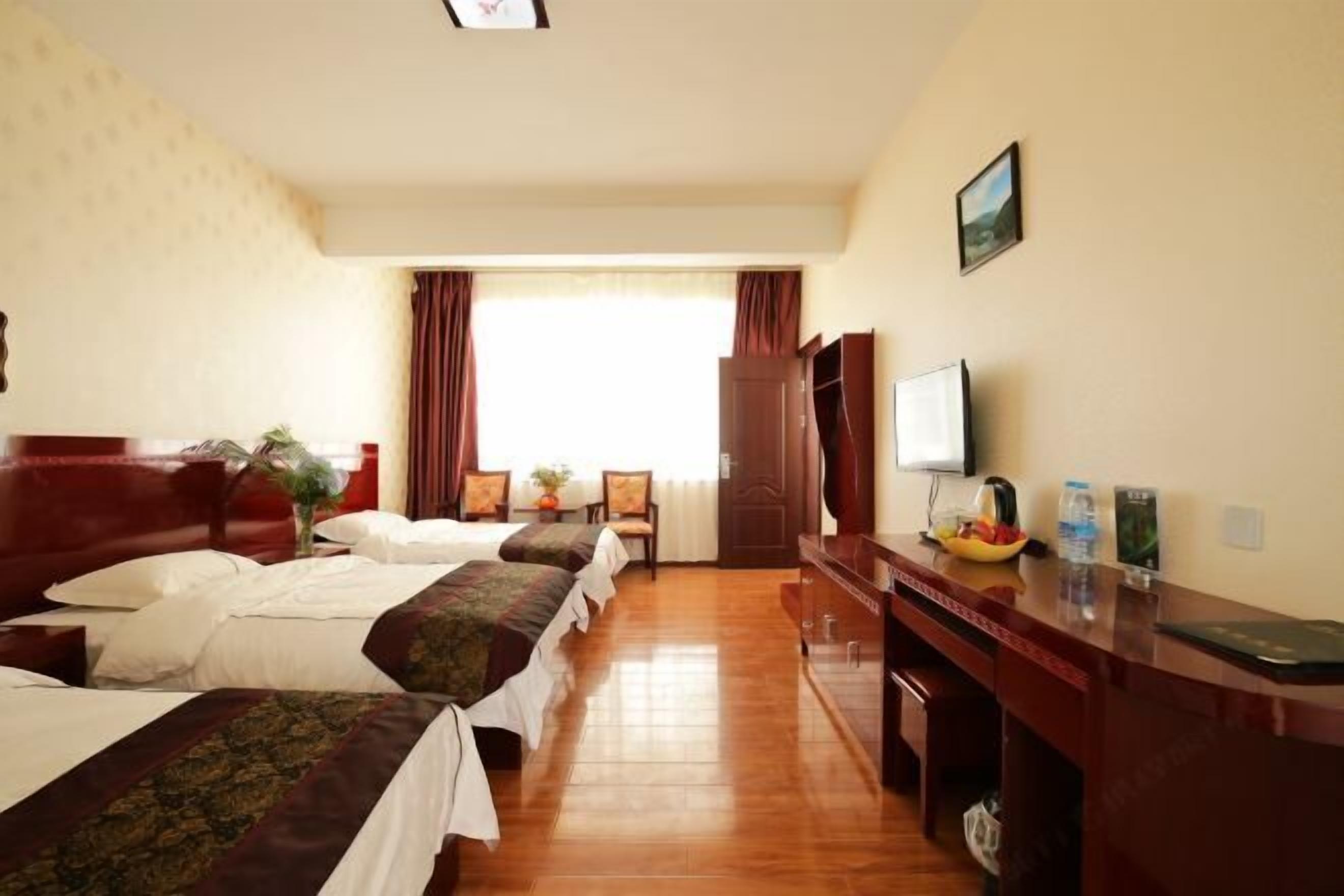 A hotel room with three beds, a desk, a television, and a window with curtains.