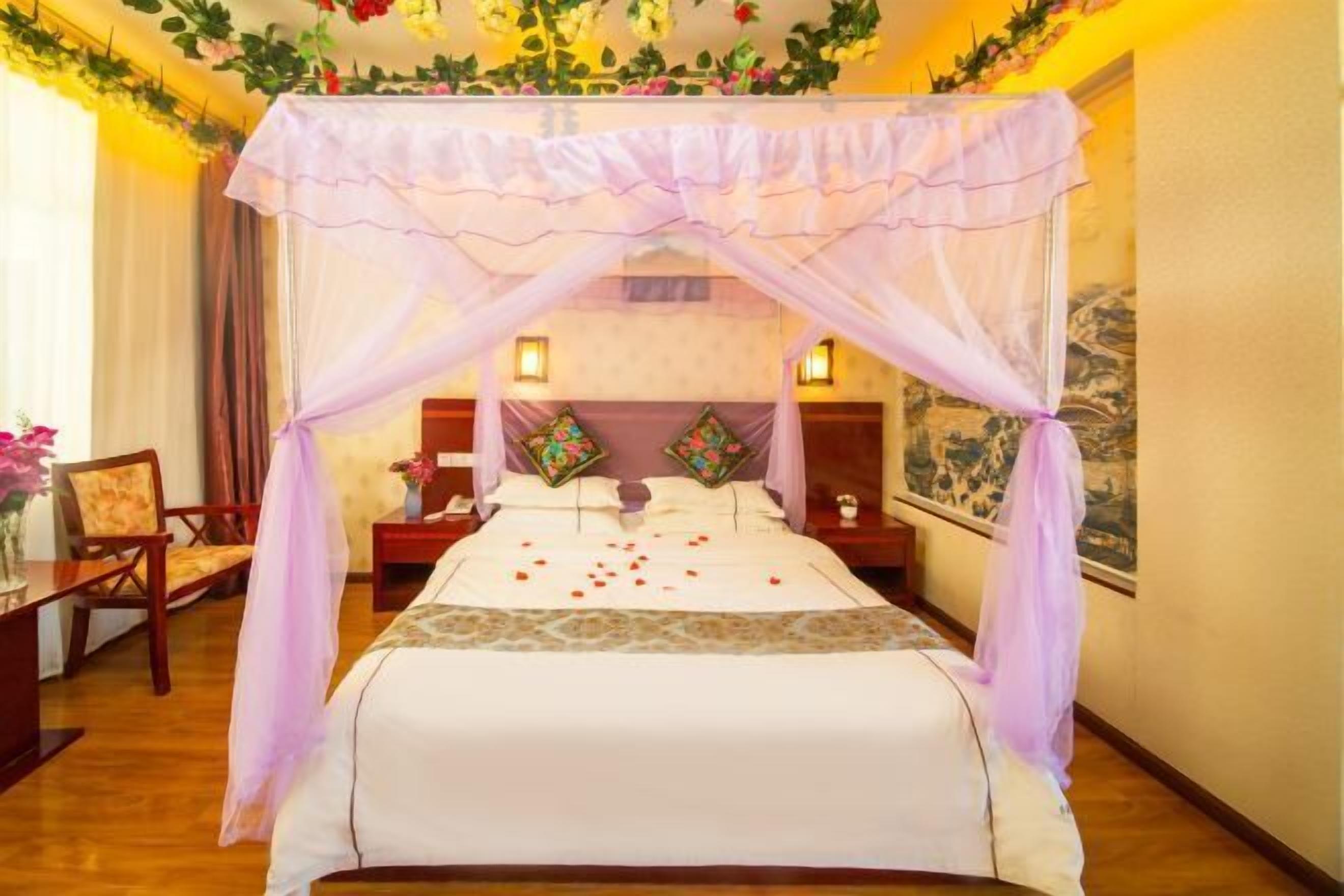 A neatly arranged bedroom with a canopy bed, floral decorations, and a painting on the wall.