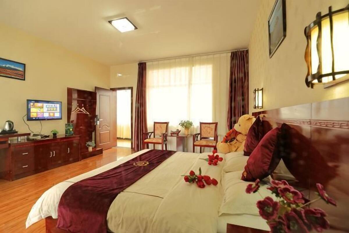 Habitació d'hotel amb llit, escriptori, cadira, televisió i finestra amb cortines.