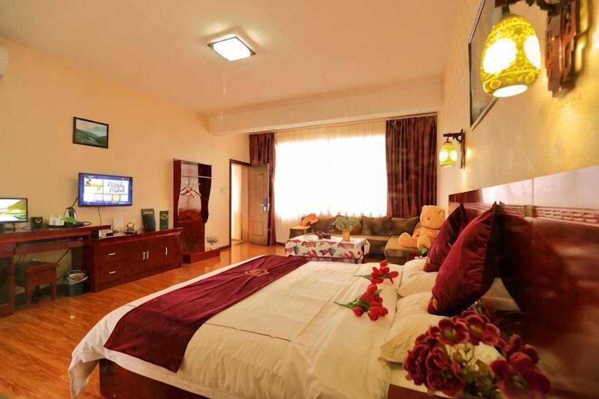 Habitació d'hotel amb un llit, una taula de treball amb un ordinador, una televisió i una finestra amb cortines.