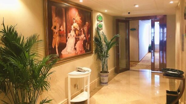Un vestíbulo de hotel con un cuadro grande, plantas en macetas, una pequeña mesa y un pasillo que conduce a otra habitación.