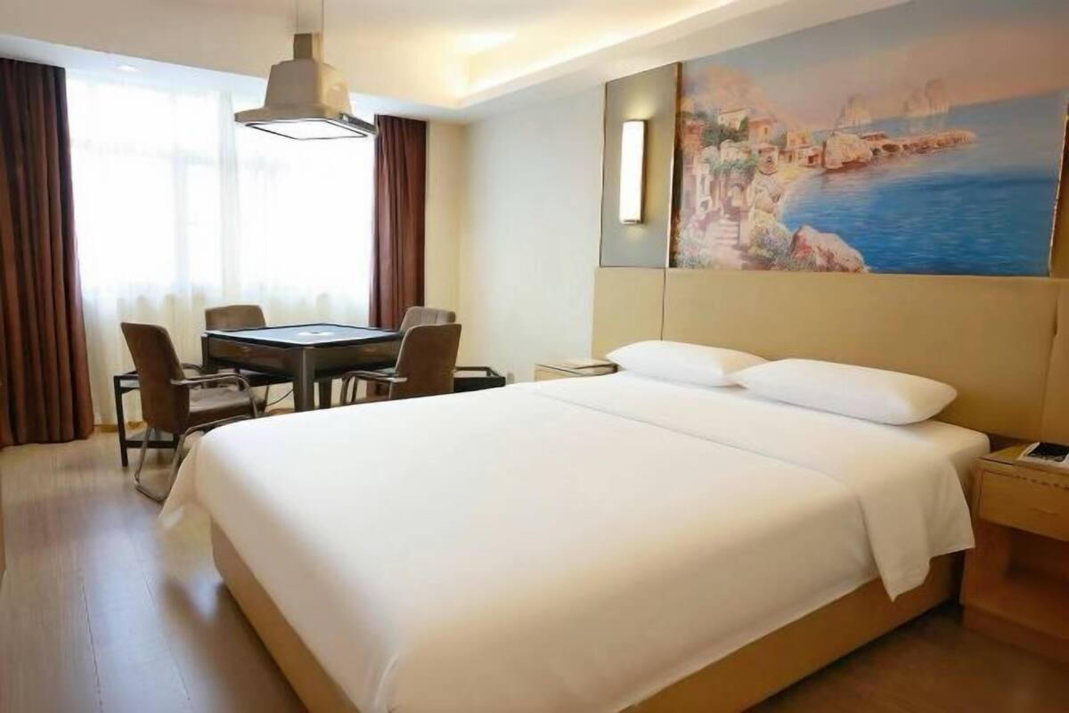A hotel room with a large bed, a desk with chairs, and a painting of a coastal scene.
