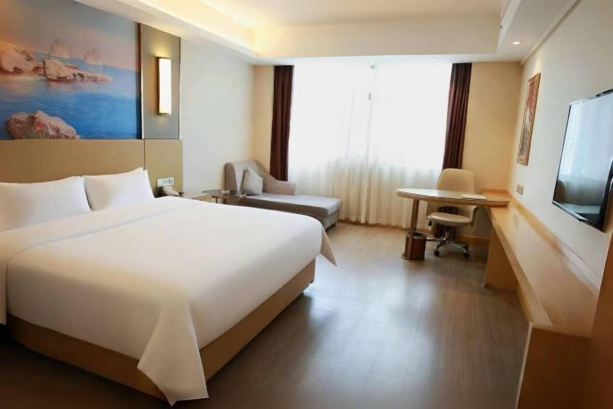 A hotel room with a large bed, a desk, a chair, a TV, and a painting on the wall.