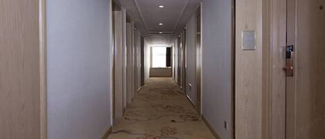 A long, narrow hotel corridor with wooden doors on both sides, a carpeted floor, and a ceiling with recessed lighting.