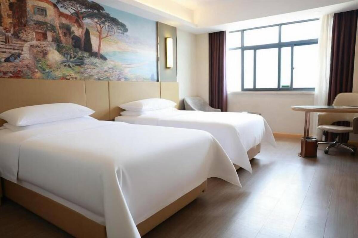 A hotel room with two beds, a desk, and a large window.