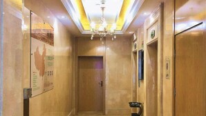 Un pasillo con candelabro, una puerta y un basurero.