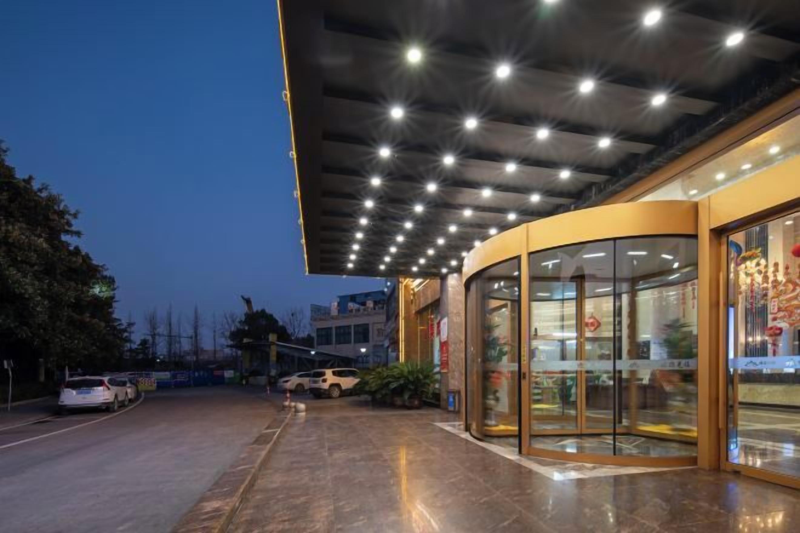 A building entrance with a curved glass door, a covered walkway, and a parking area.