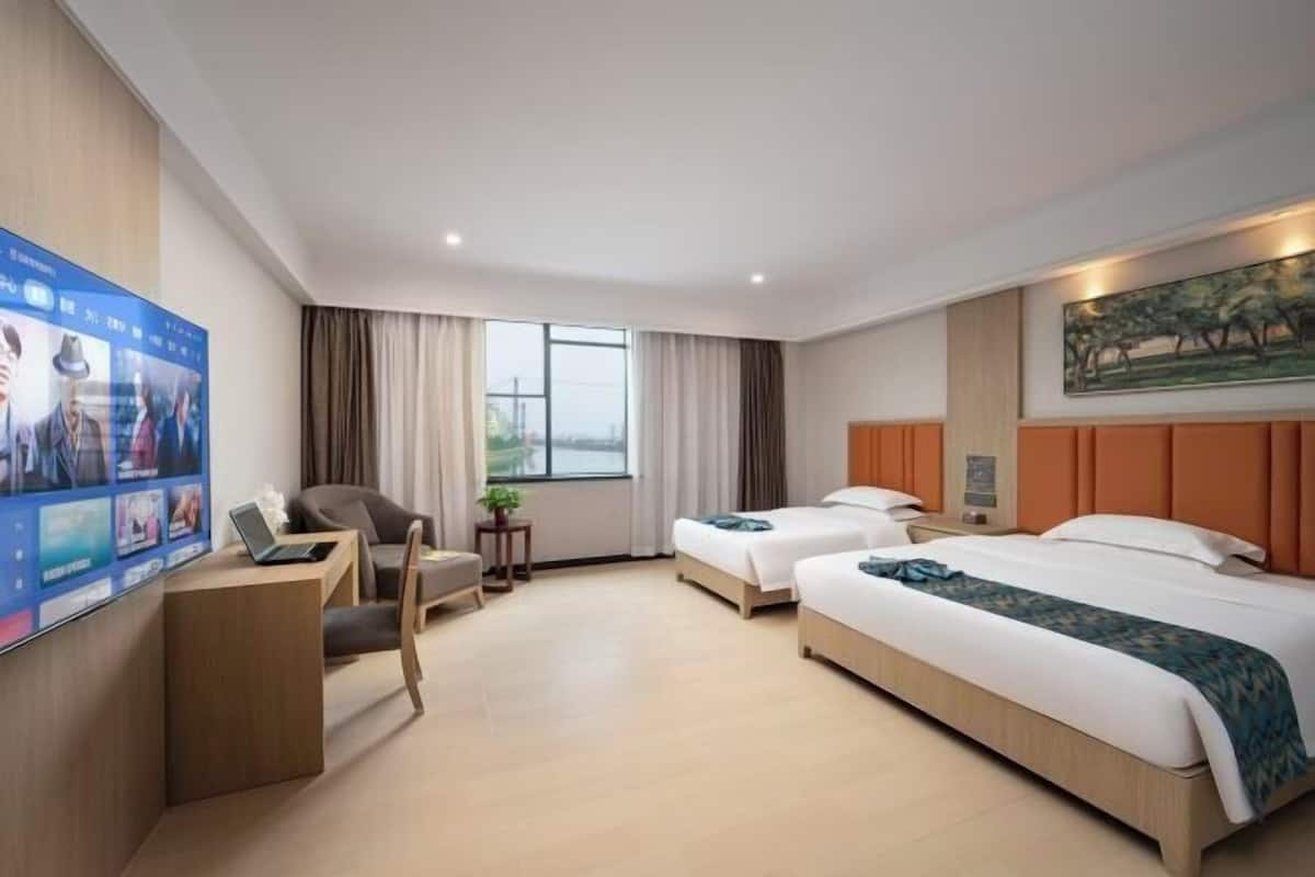 A hotel room with two beds, a desk with a laptop, a chair, a TV, and a painting on the wall.