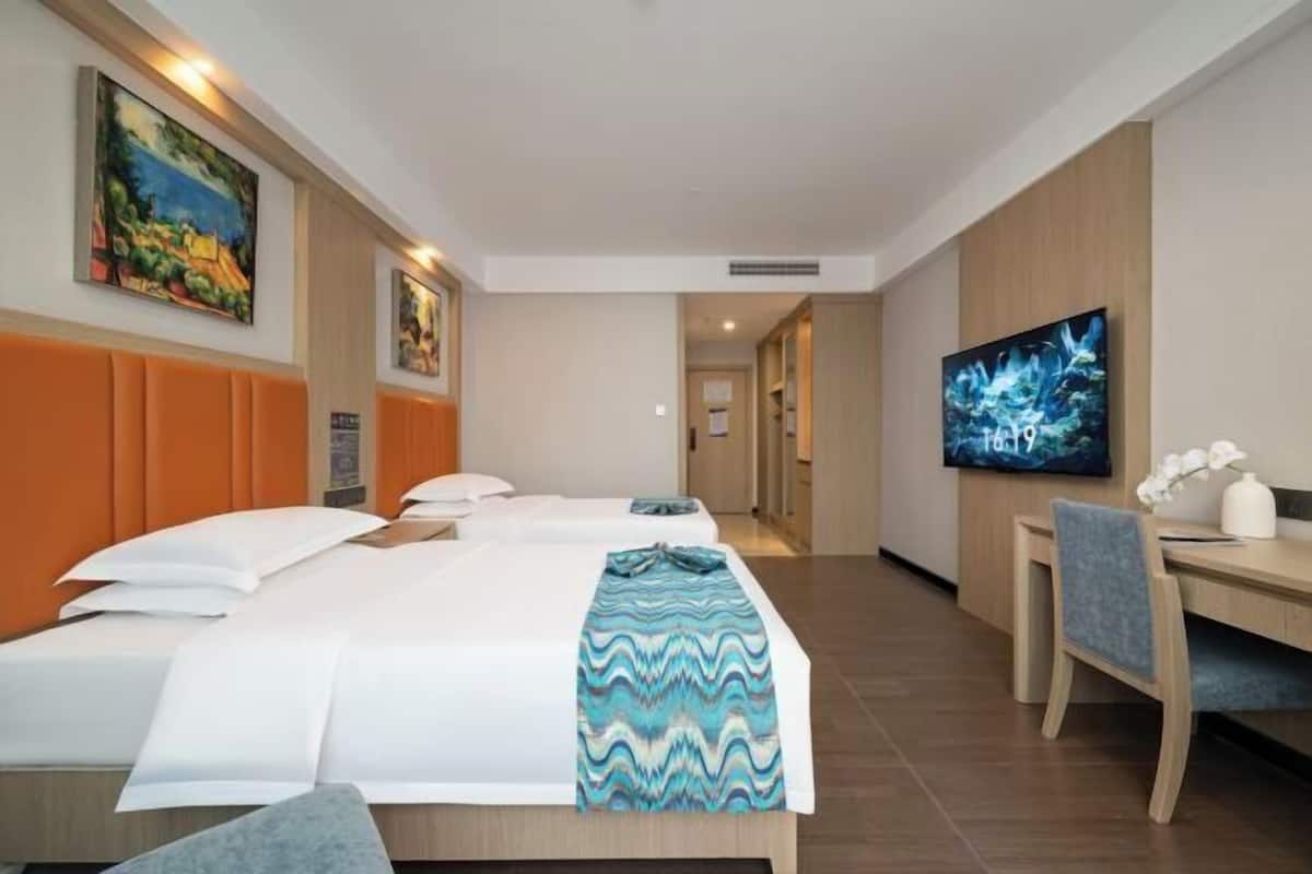A hotel room with two beds, a desk, and a TV.