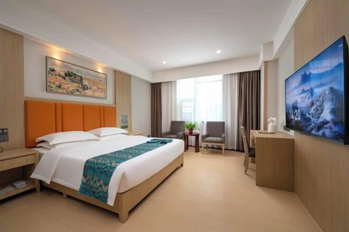 A hotel room with a large bed, a desk, a chair, a television, and a painting on the wall.