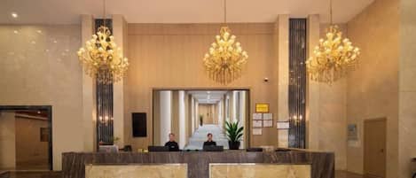 A hotel reception area with a marble reception desk, two chandeliers, and a large mirror.