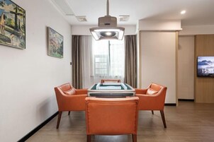 Habitación de hotel con mesa de billar, sillas de cuero naranja, una lámpara de techo y televisor en la pared.