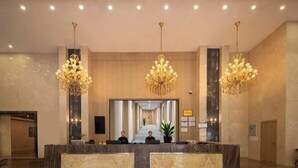 Ein Hotel-Empfangsbereich mit einem Marmor-Empfangstresen, drei Kronleuchtern und einem Korridor zu den Zimmern.