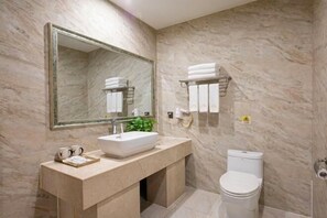 A bathroom with a marble wall, a large mirror, a sink with a vessel basin, a toilet, and a towel rack.