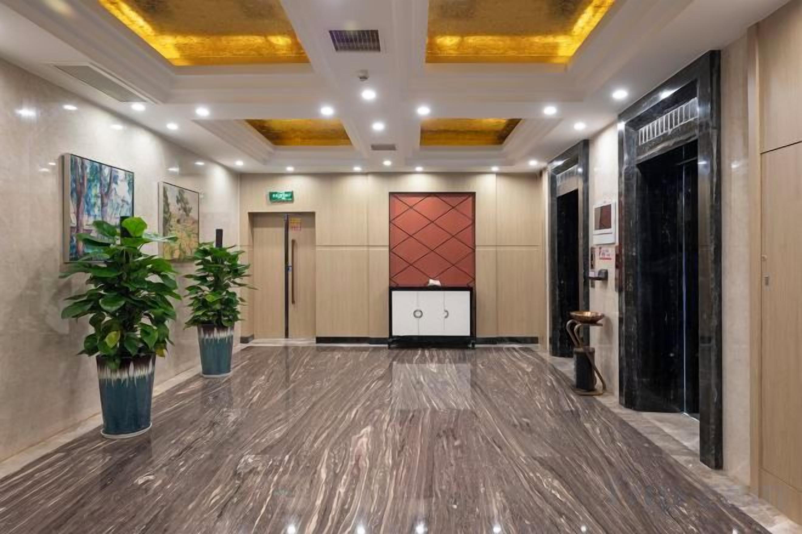 Una hall d'albergo con pavimento in marmo, una reception e un pannello decorativo rosso al muro.
