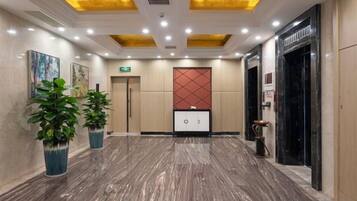 Una hall d'albergo con pavimento in marmo, una reception e un pannello decorativo rosso al muro.