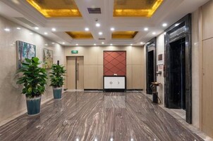 A hotel lobby with a marble floor, a reception desk, and a red decorative panel on the wall.