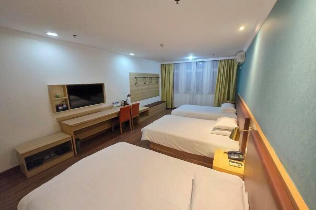 Ein Hotelzimmer mit zwei Einzelbetten, einem Schreibtisch mit Stuhl, einem Fernseher und einem Kleiderschrank.