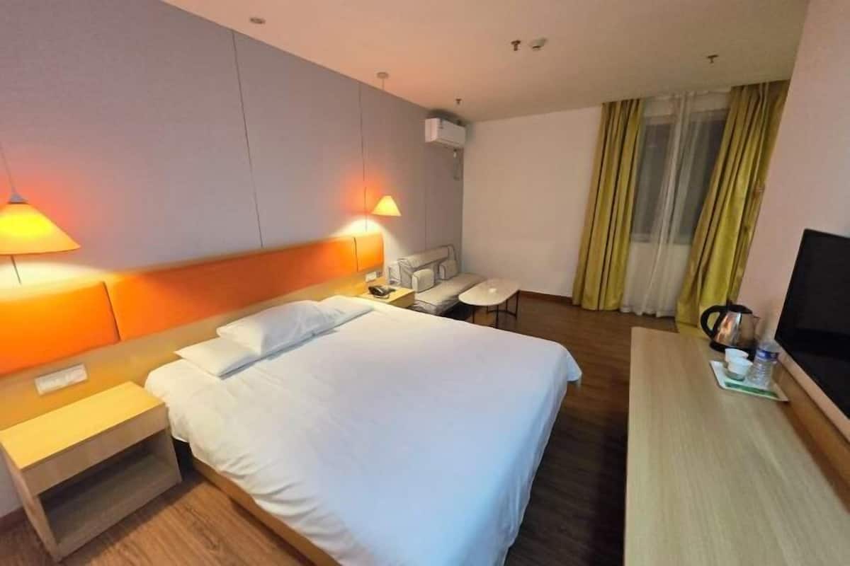 Ein Hotelzimmer mit Bett, Nachttischen, Schreibtisch, Stuhl, Fernseher und einem Fenster mit Vorhängen.