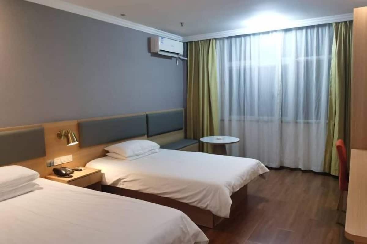 Ein Hotelzimmer mit zwei Betten, einem Nachttisch mit Lampe, einem kleinen runden Tisch und einem Fenster mit Vorhängen.