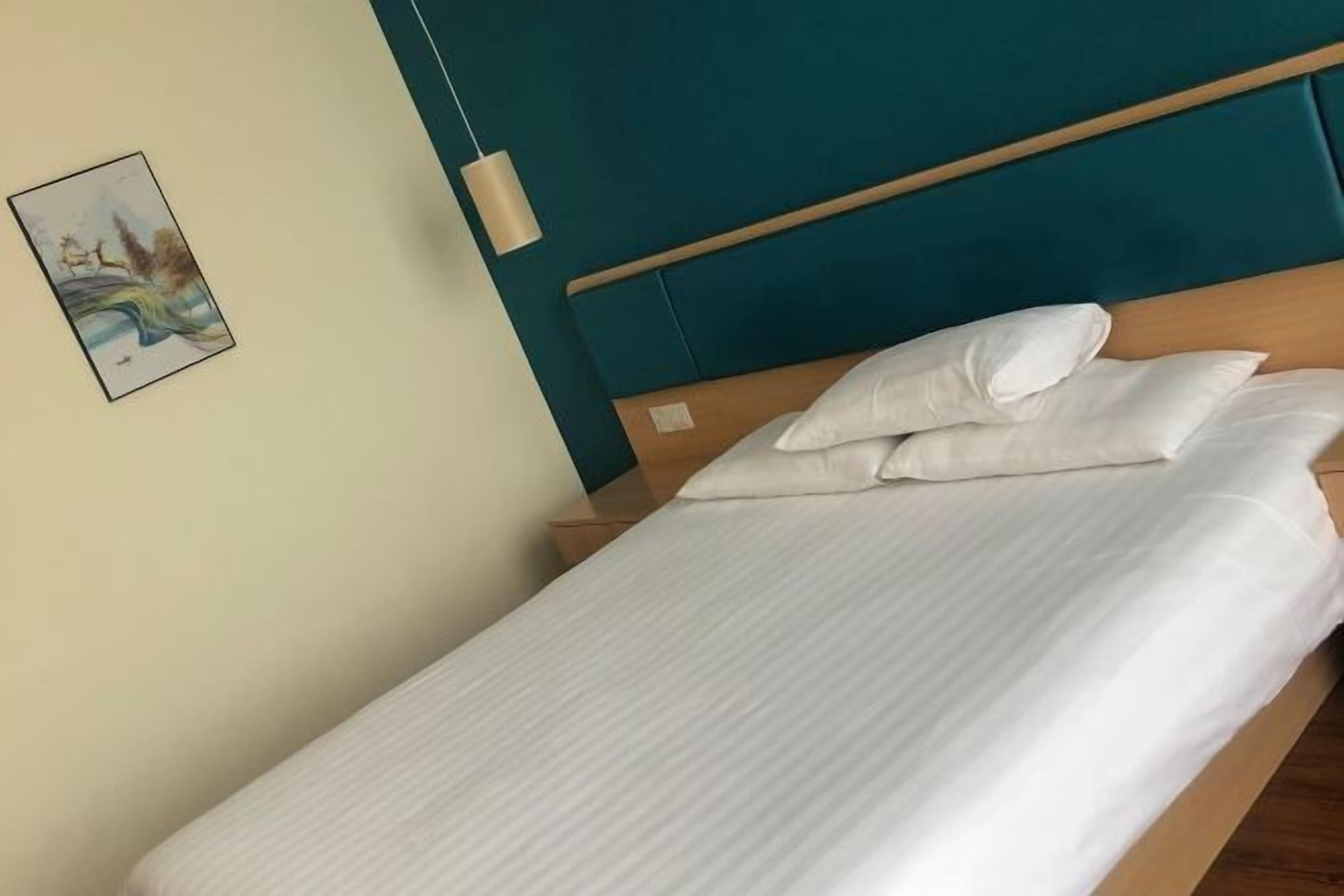 A neatly made bed with white linens and pillows, a teal headboard, and a wall-mounted light fixture.