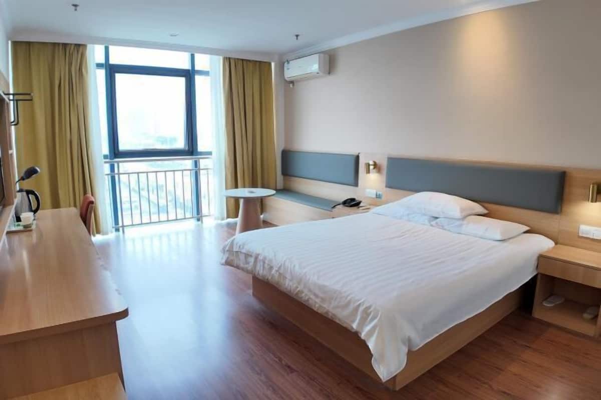 Ein Hotelzimmer mit einem großen Bett, einem Schreibtisch, einem Sessel, einem kleinen Tisch und Blick ins Freie durch ein Fenster.