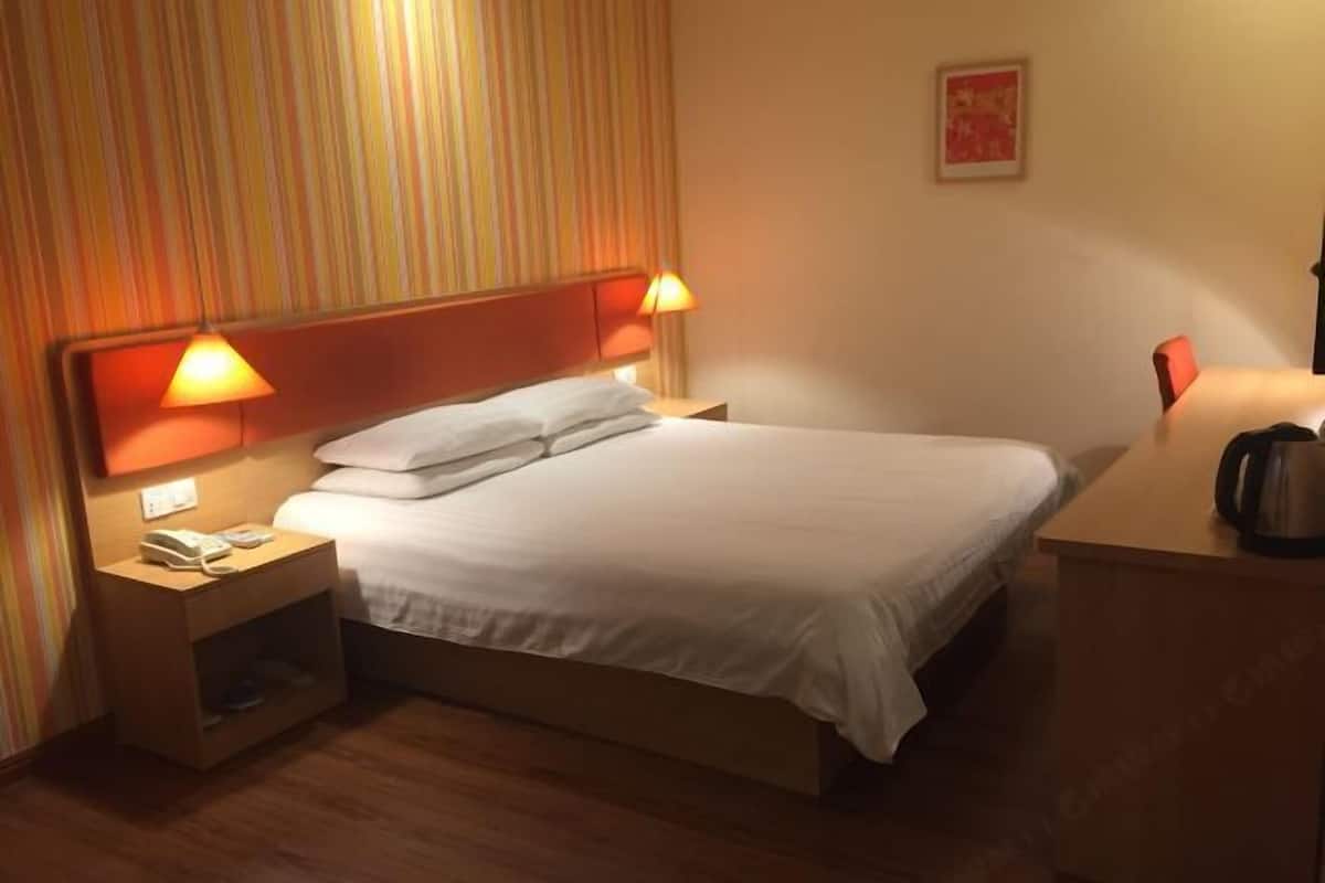 Ein Hotelzimmer mit einem Einzelbett, zwei Nachttischlampen, einem Nachttisch mit Telefon und einer Kaffeemaschine auf dem Schreibtisch.