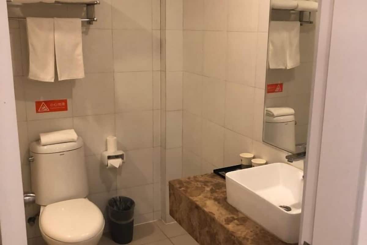 Ein kleines Badezimmer mit Toilette, Waschbecken und Spiegel. Über der Toilette befindet sich ein Handtuchhalter und daneben ein Mülleimer.