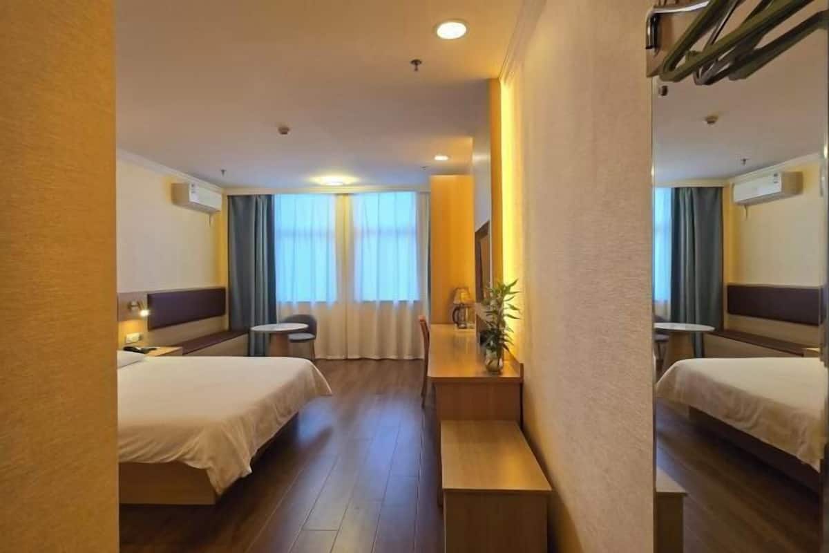 Ein Hotelzimmer mit zwei Betten, einem kleinen Tisch mit einer Lampe, einem Fenster mit Vorhängen und einer Pflanze.