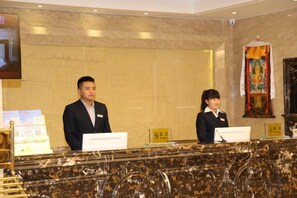A reception desk with two staff members, a marble counter, and a wall-mounted television. - hide bdr hotel (Diebu)