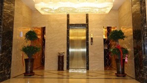 A lobby with a marble floor, a central elevator, and two potted plants with red ribbons. - hide bdr hotel (Diebu)