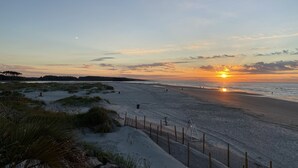 Una spiaggia con una recinzione di legno, dune erbose e un tramonto sull'oceano.
