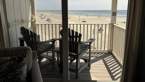 Un balcone con sedie e tavolo in legno, affacciato su una spiaggia con ombrelloni e persone.
