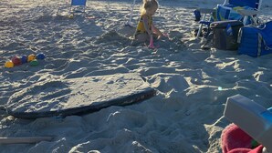 Una spiaggia sabbiosa con un bambino che gioca, sedie a sdraio e ombrelloni.