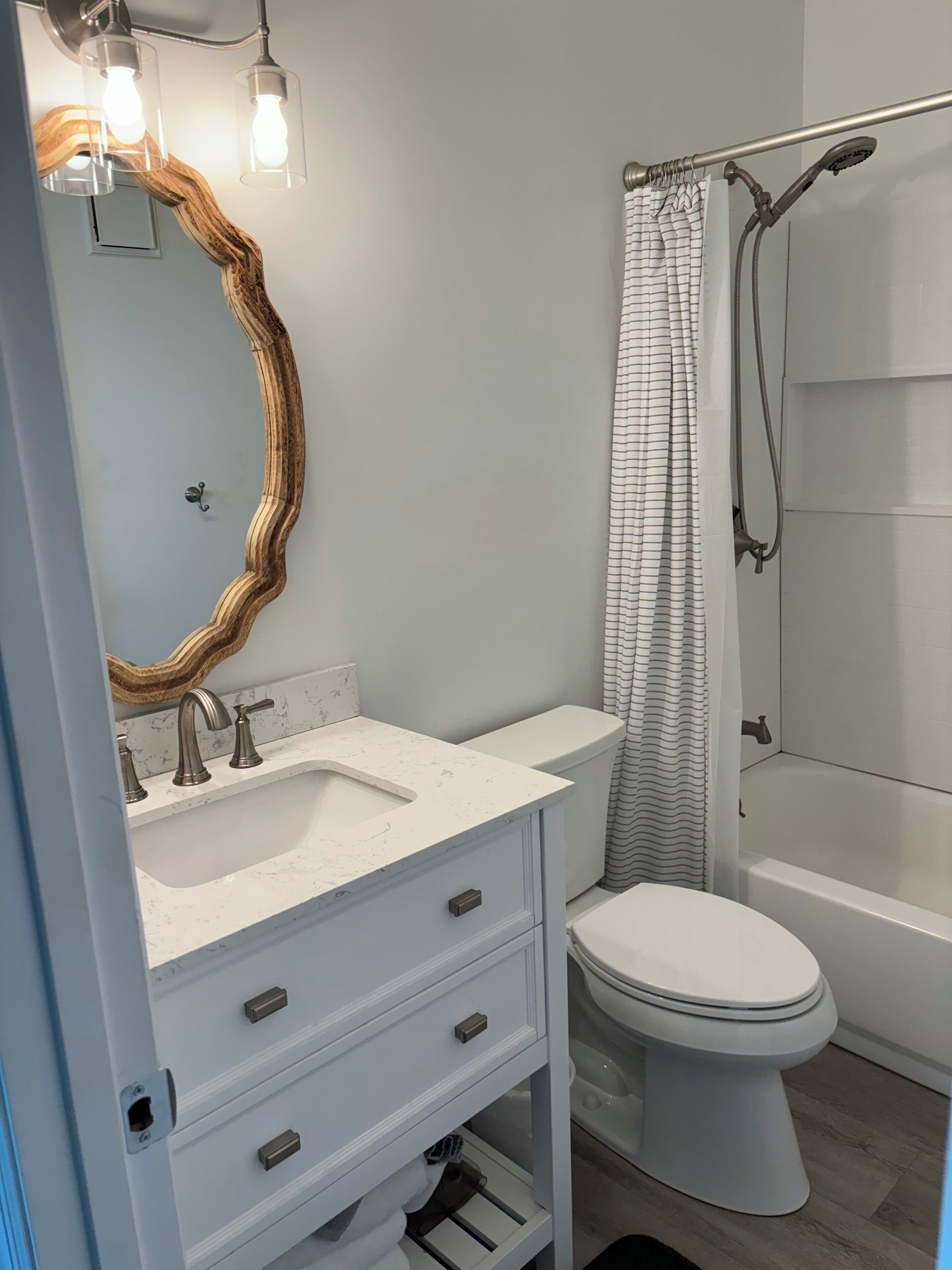 Een badkamer met een wit wastafel, meubel en toilet. Er is een douche met gordijn en een spiegel met houten lijst.