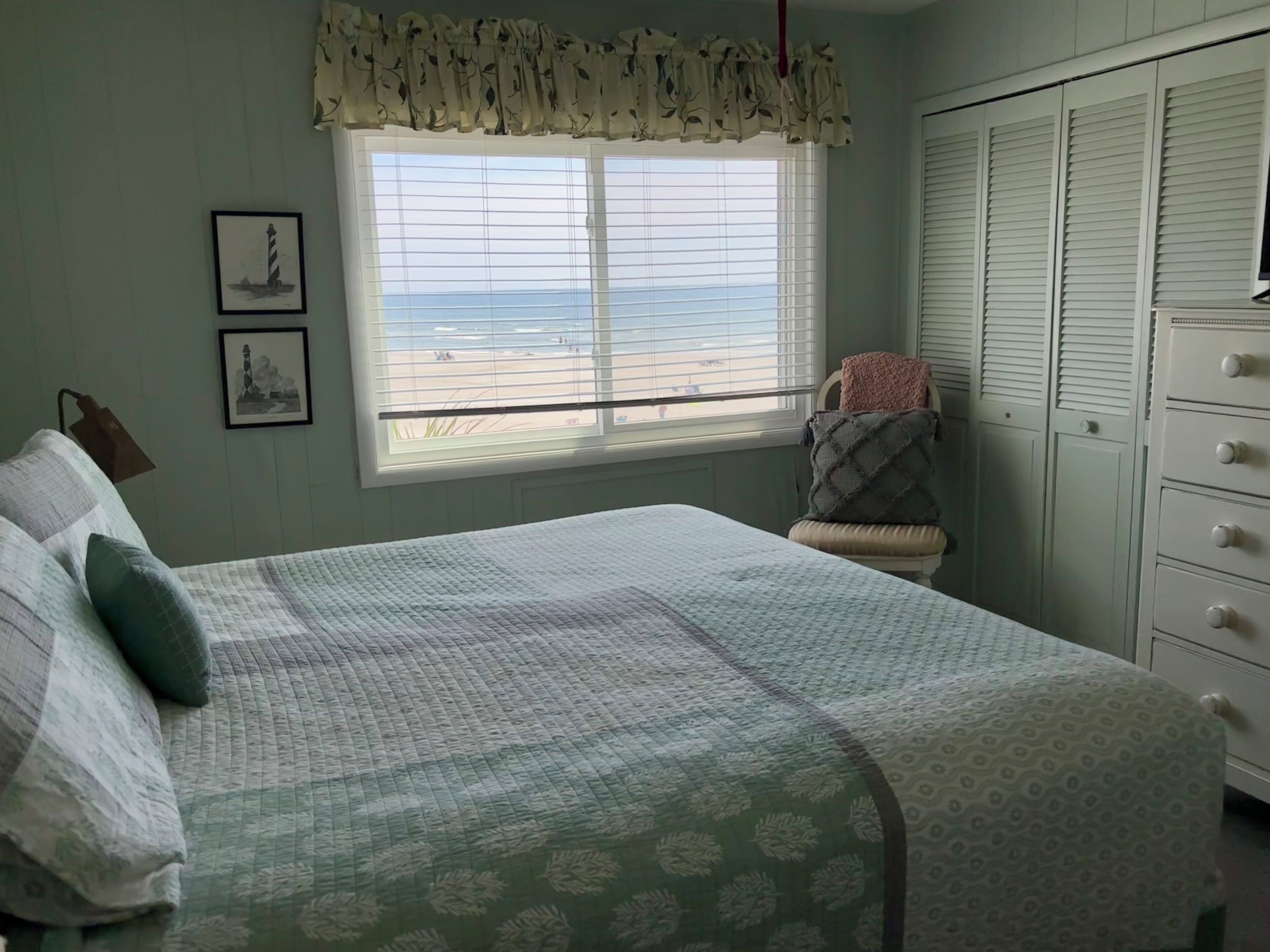Quarto com cama, janela com vista para a praia, guarda-roupa e abajur.