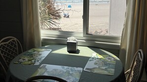 A dining area with a table set for two, a window with a view of the beach, and a ceiling fan. - Oceanfront Condo Clean and Stocked - best view,  steps from beach (North Myrtle Beach)
