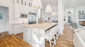 A modern kitchen with white cabinetry, a central island, stainless steel appliances, and pendant lighting. - Private Pool, Lake Views , 6 Seat Golf Cart/LSV | Lake District Home in Watercolor, FL (Santa Rosa Beach)