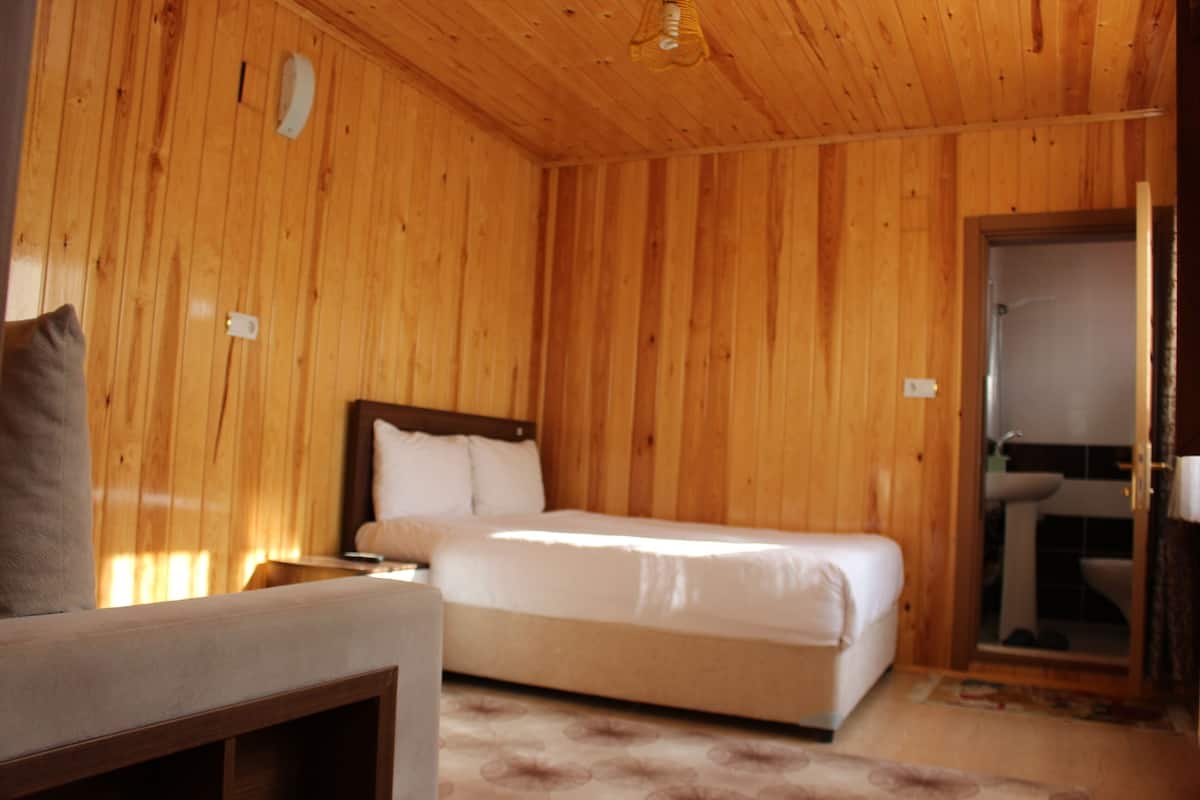 A wooden-paneled room with a bed, a bedside table, and a bathroom visible through an open door.
