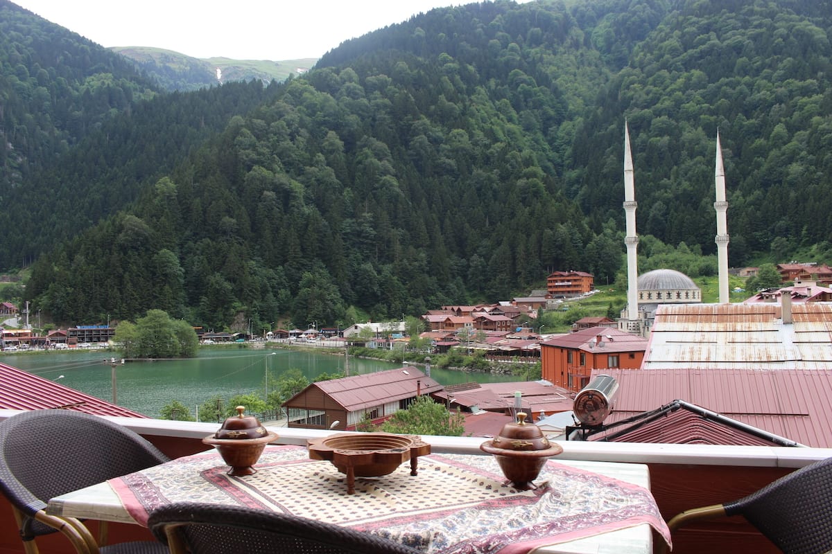 A terrace with a table set for dining, overlooking a lake and a mosque with two minarets.