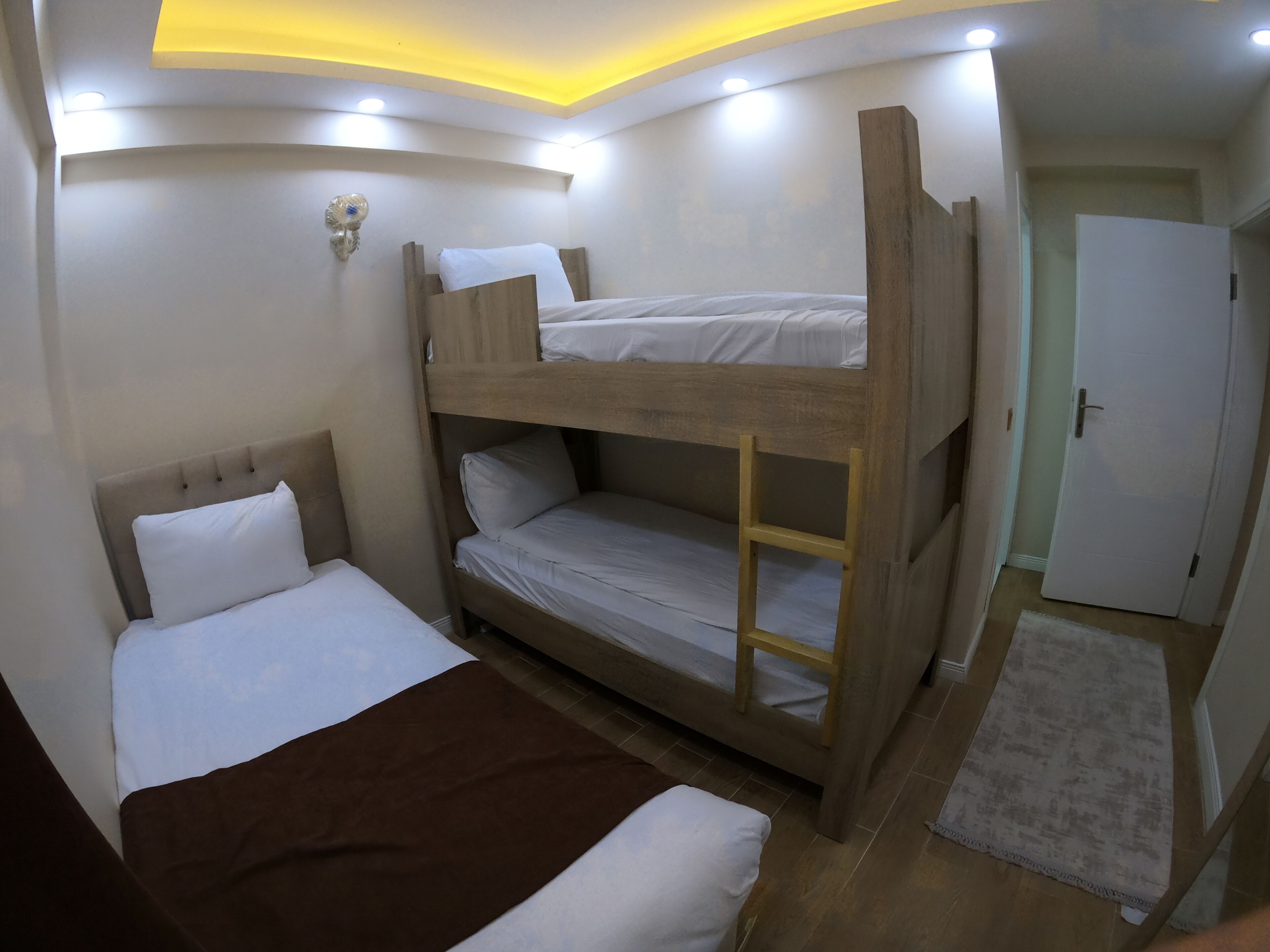 A bunk bed room with a wooden headboard, a white mattress, and a brown blanket. There is a small wooden ladder attached to the bunk bed.