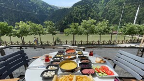 A table set with a variety of dishes, including French fries, bread, and vegetables, overlooking a scenic lake with mountains in the background. - Uzungol Adiloglu Apart (Çaykara)